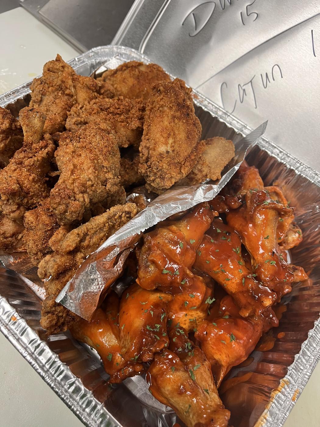 Two foil catering trays of fried chicken and sauced wings
